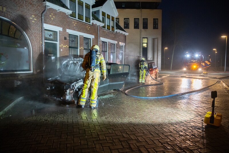 Twee brandweerlieden blussen beide een auto in de Ooievaarstraat, waar vanmorgen maar liefst vier auto's in brand werden gezet.
